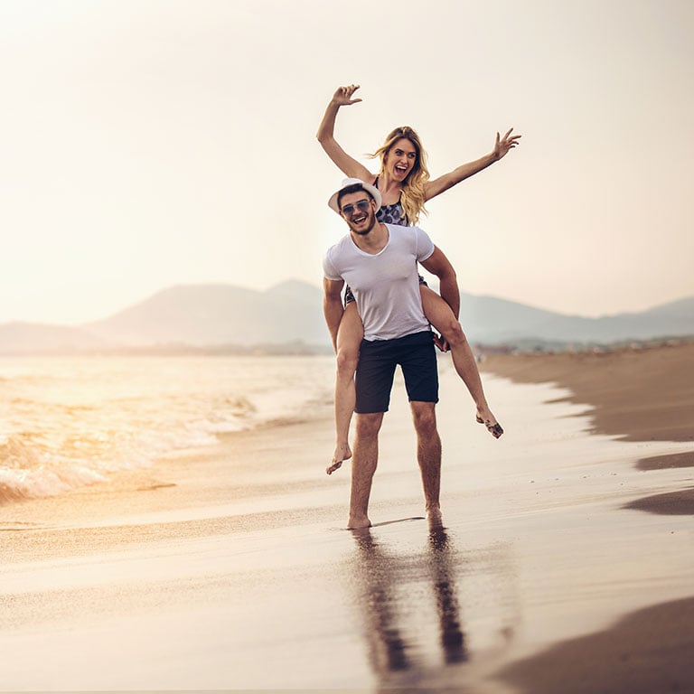 Young active couple on the beach illustrating the non-invasive nature of CoolSculpting with no down time (unlike liposuction)